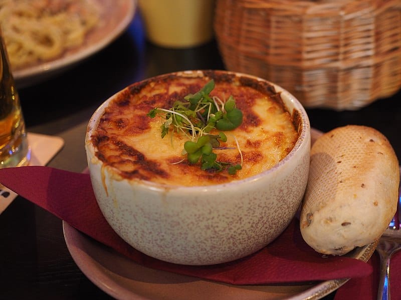 An individual serving of shepherd's pie with a grainy roll on a red plate.