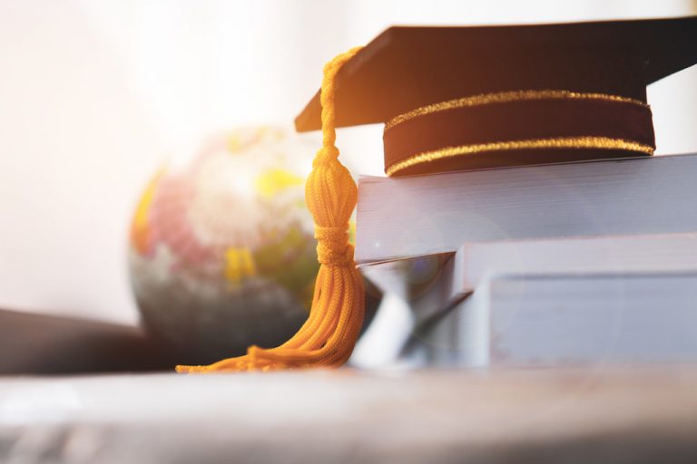 A photo of a graduation cap on top of a stack of books.