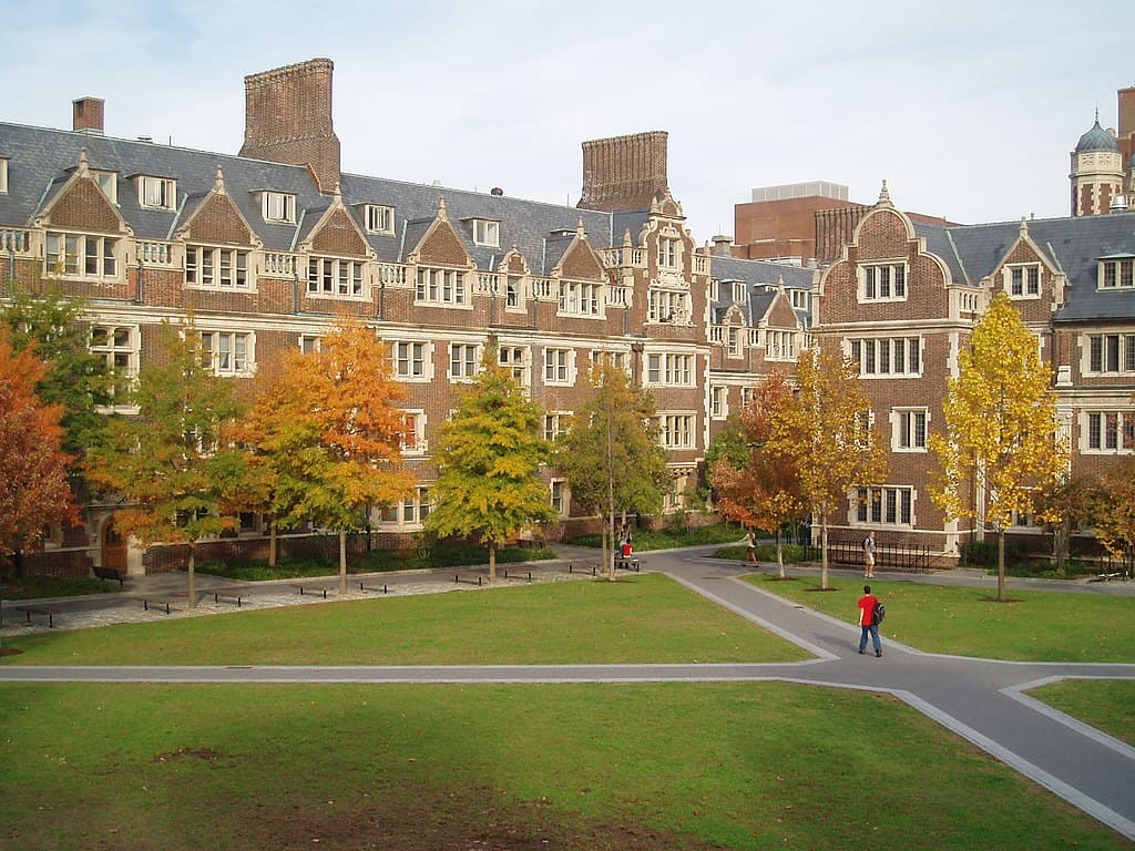 Three-storey brick buildings ring a green lawn, quartered by a concrete path. (UPenn campus)