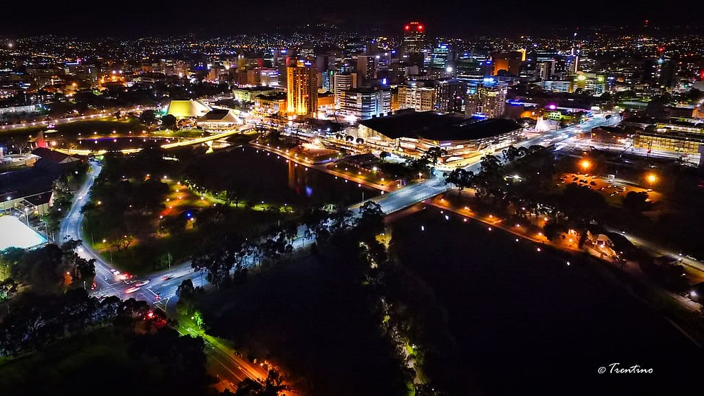 Adelaide at night: a maze of multicoloured, lit city streets, the downtown's tall buildings at the centre, and the suburbs' twinkling lights stretching out in the rearground.