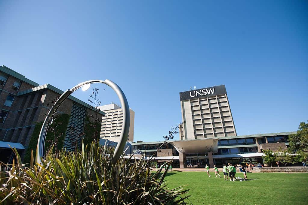 The Library Lawn at the University of South Wales - there is a sculpture with greenery in the foreground, a soccer team on the lawn, and the library building in the distance.