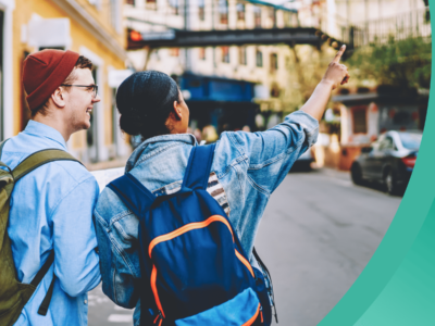 Two students walk along an urban street, wearing backpacks and fall clothing