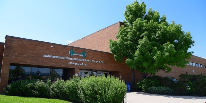 A multi-storey brick building framed by trees. (MITT, Manitoba)