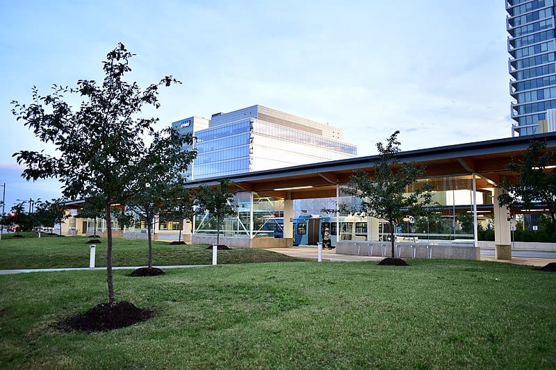 A transit station with a train at it is set on a green lawn with tall office buildings behind it (Vaughan, Ontario)