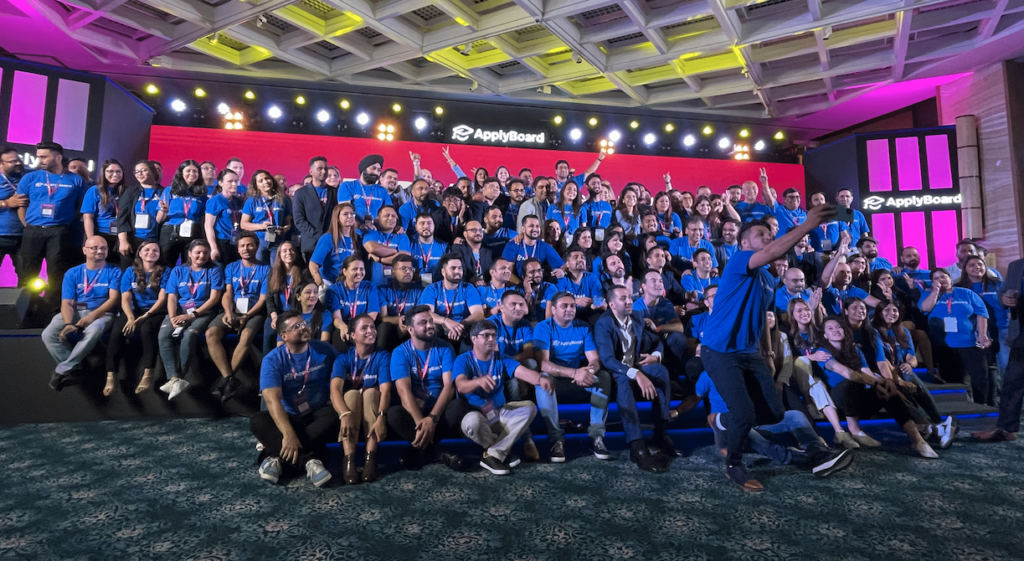 A high-quality photo of the ApplyBoard team at TRW 2022, featuring many dozens of people all wearing blue ApplyBoard t-shirts.