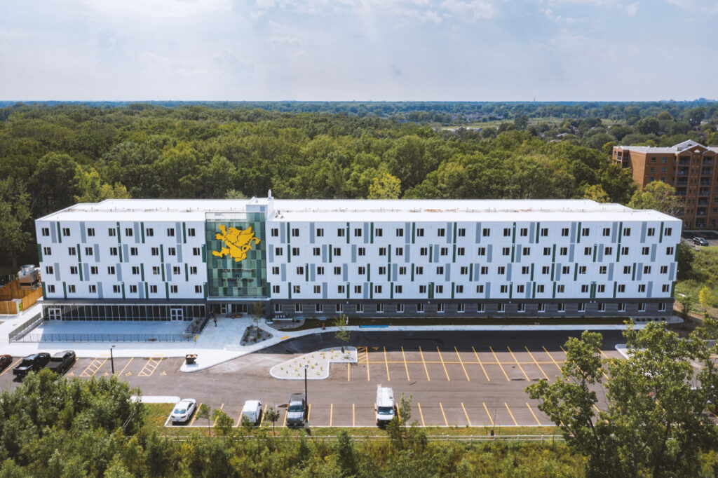 A photo of the white GEM Residence building for international students, surrounded by green trees on a sunny day.