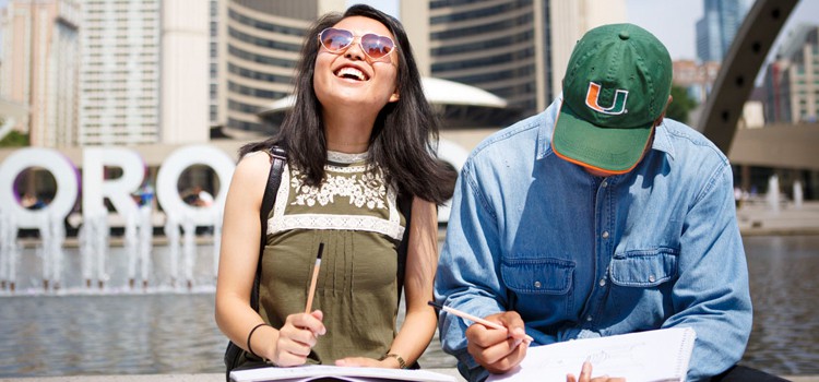 Two students sit near the reflecting pool and TORONTO sign outside of Toronto's City Hall