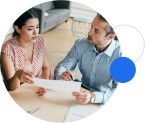 A man and a woman sit at a desk and hold a piece of paper together.