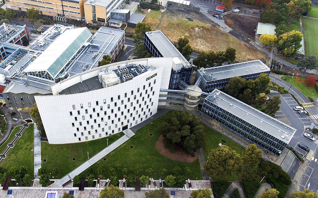 An aerial view of Deakin University's Building C - a tall white building on a green lawn, from which three smaller grey buildings fan out from its far right wall like a starburst. The Deakin campus extends on all sides.