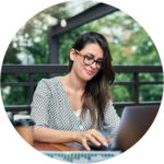 A young woman sits on a patio at a desk and types on a laptop computer