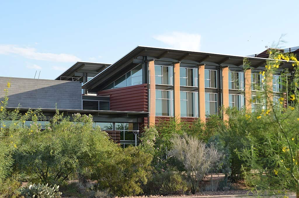 A modern multistorey building with large windows rises from behind desert bushes on the Arizona State University - Mesa campus.