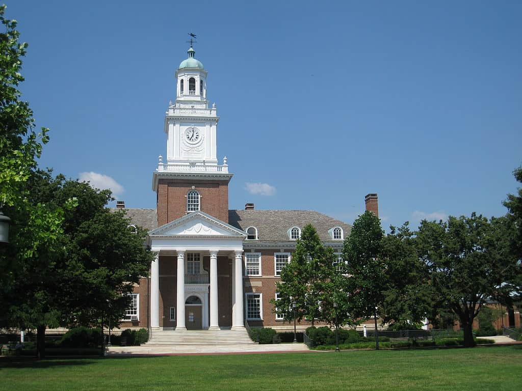The Johns Hopkins University campus: a green lawn edged by trees with a stone and brick academic building in the centre