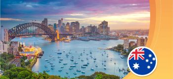 A seaside view of an Australian city; a curved bridge over a blue bay and a downtown skyline with tall towers.